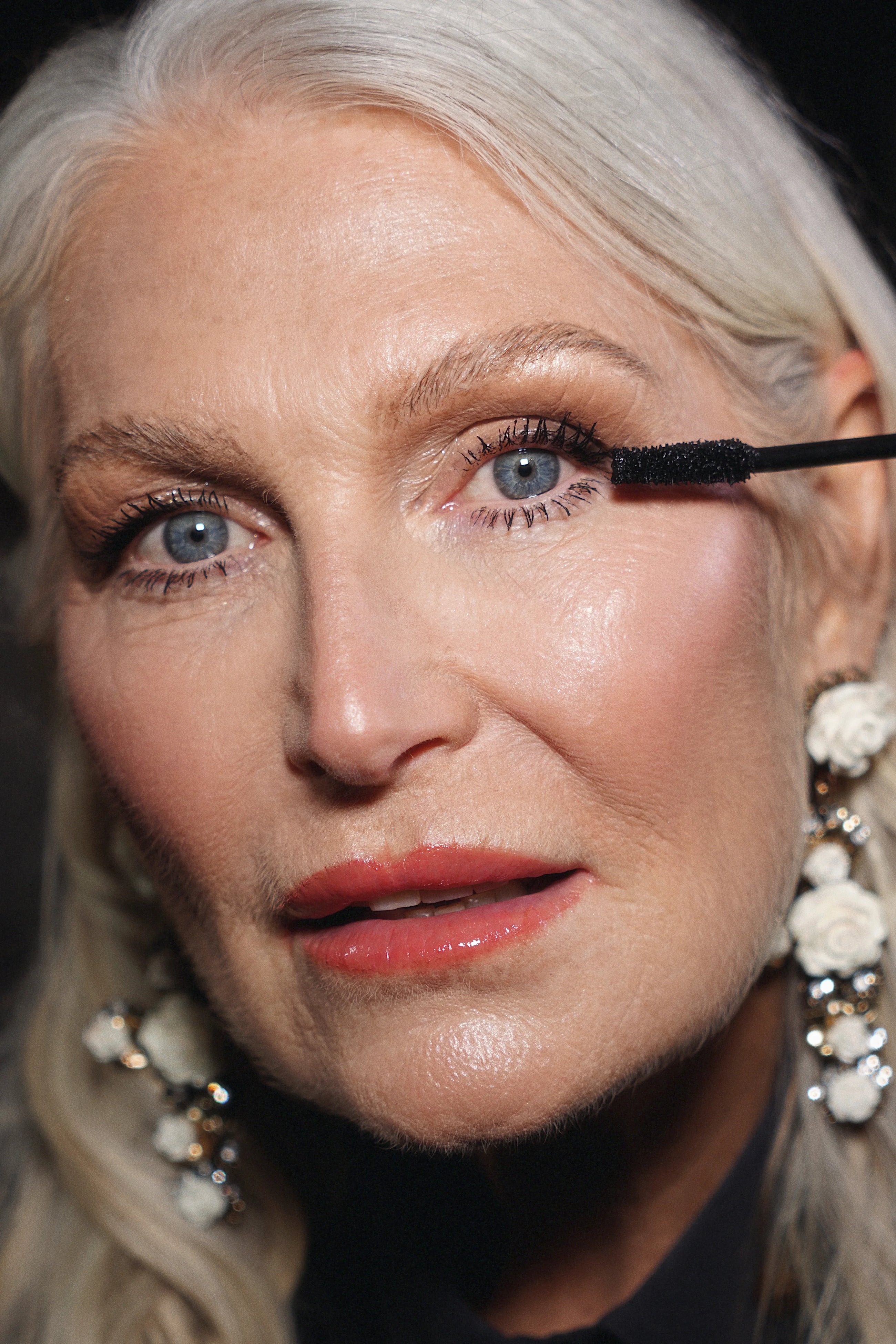 Close-up of a woman applying Qudos I Wand You water resistant mascara with a brush.