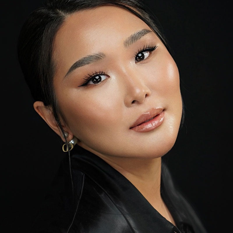 Asian woman stood side-on while staring at camera with natural face makeup and eye makeup applied against black background