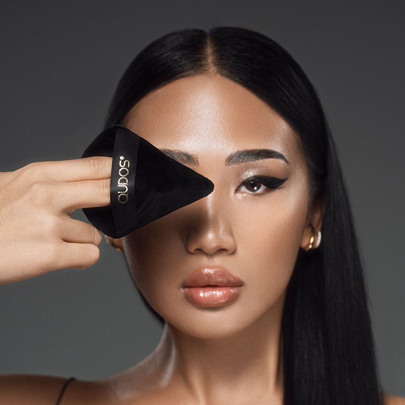 Asian woman with natural face makeup and eyeliner staring at camera with Synergy face puff in front of her right eye