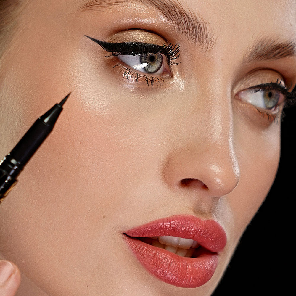 Extreme close up of woman looking away from camera with top section of Qudos I Line you eyeliner held below her right eye