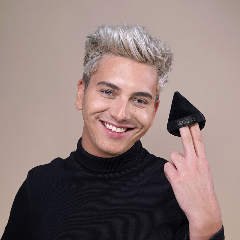 Man with silver-styled hair smiling at camera while holding Synergy face puff with his left hand with Qudos name on display