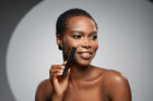 Dark-skinned woman staring to the left while holding I Wand You mascara against her right cheek 