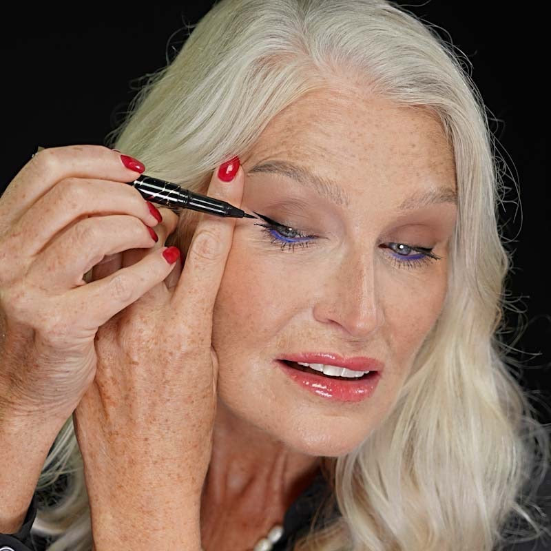 Older woman applying Qudos I Line You eyeliner while looking down away from camera 