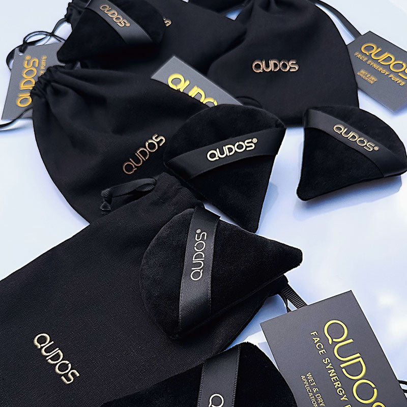 Small black pouches and Synergy face puffs laid out on table surface with QUDOS written on each of them