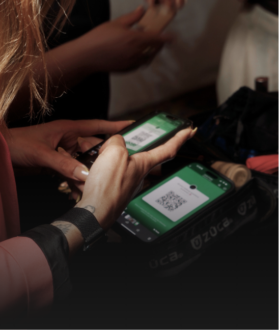 Two hands holding smartphones with QR codes displayed, interacting with a device on a table.