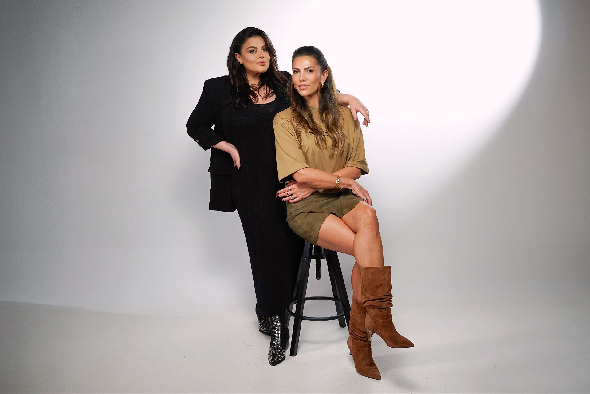 Qudos director Andra sat on stool with director Ana-Maria stood behind her with arm on shoulder, both smiling at the camera 