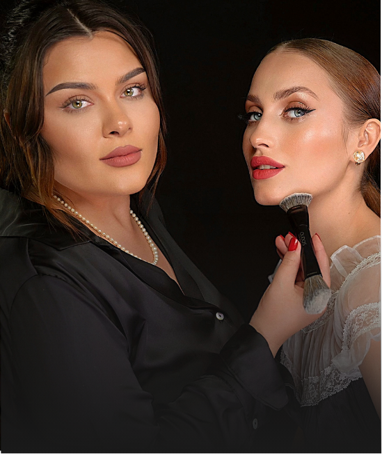Ana Maria, founder of Qudos, applying makeup to the other with a brush, against a black background.
